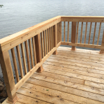 A wooden deck with railing and water in the background.