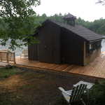 A cabin with a dock and chair on the shore of a lake.