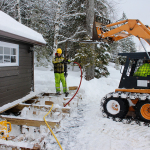 A man in yellow jacket using a hose to connect the hose to a backhoe.