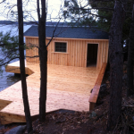 A cabin on the water with a dock in front of it.